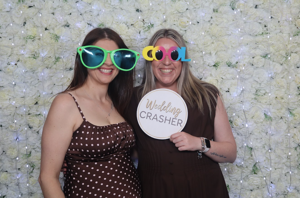 Guests posing with props in front of white flower wall backdrop