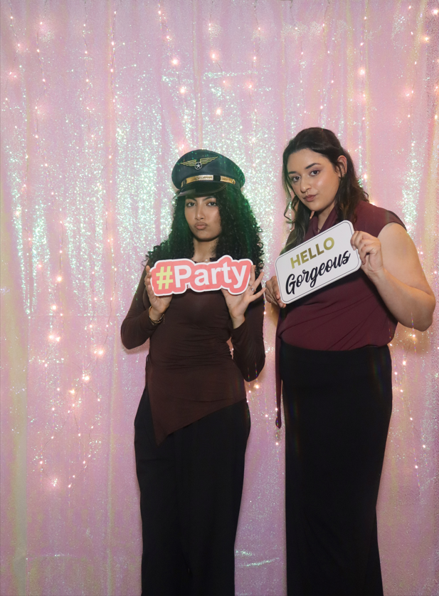 Guests posing with party signs in front of shimmer backdrop